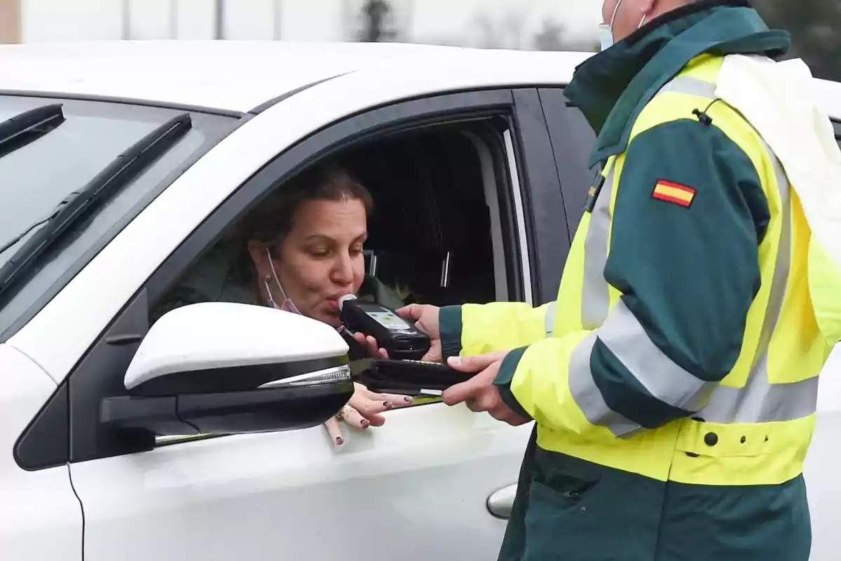 Una mujer en un coche blanco sopla en un alcoholímetro sostenido por un agente de tráfico con uniforme de alta visibilidad. Una mujer en un coche blanco sopla en un alcoholímetro sostenido por un agente de tráfico con uniforme de alta visibilidad.