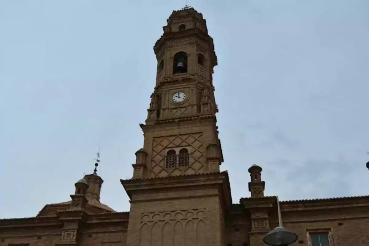 Torre de una iglesia de ladrillo con un reloj en la parte superior bajo un cielo nublado ubicada en Navarra. Torre de una iglesia de ladrillo con un reloj en la parte superior bajo un cielo nublado ubicada en Navarra.