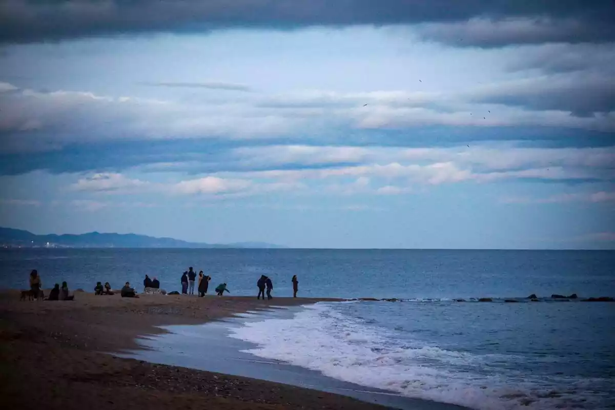 Imagen de un atardecer en la playa de la Barceloneta con varias personas al lado del mar Imagen de un atardecer en la playa de la Barceloneta con varias personas al lado del mar