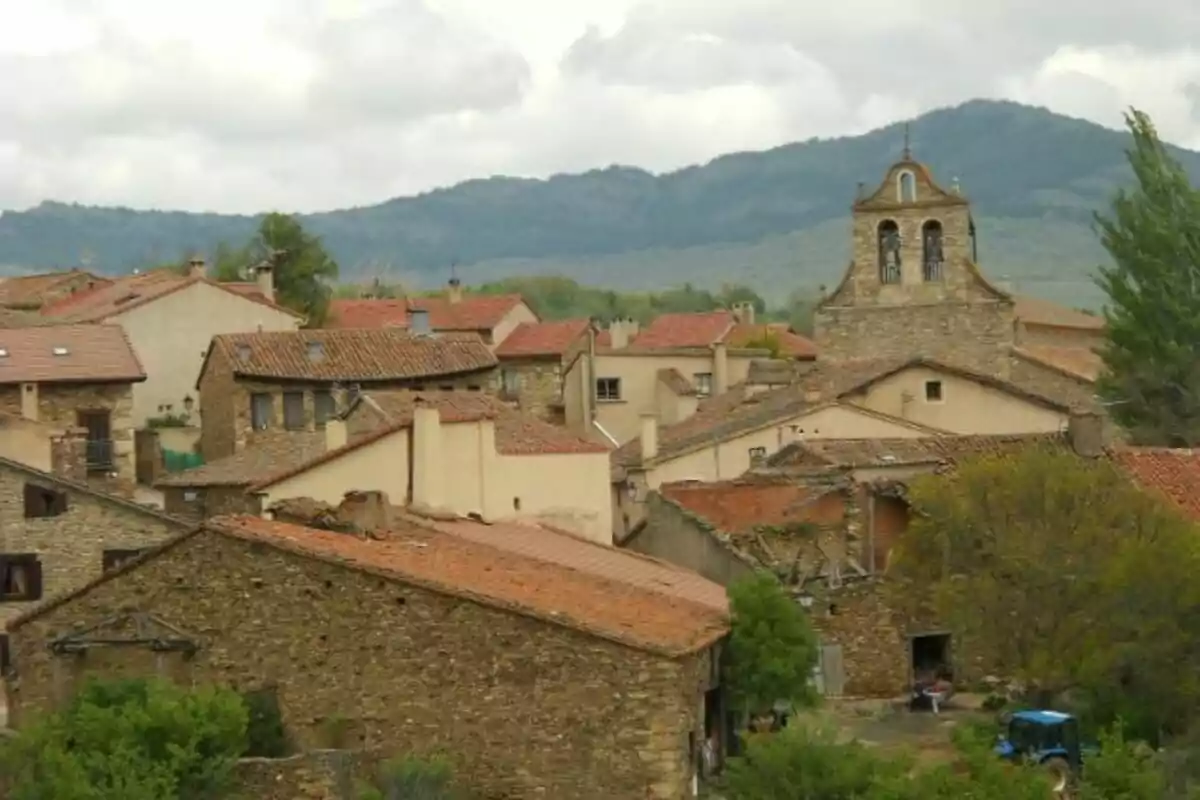 Vista de un pueblo con casas de piedra y techos de teja roja rodeado de montañas y vegetación.