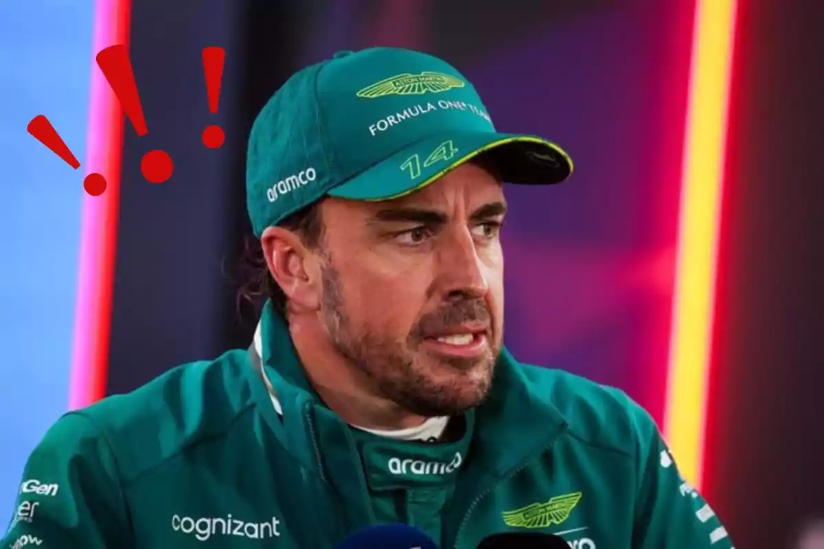Un hombre con gorra y chaqueta verde de un equipo de automovilismo, con un gesto serio y signos de exclamación rojos sobre su cabeza. Un hombre con gorra y chaqueta verde de un equipo de automovilismo, con un gesto serio y signos de exclamación rojos sobre su cabeza.