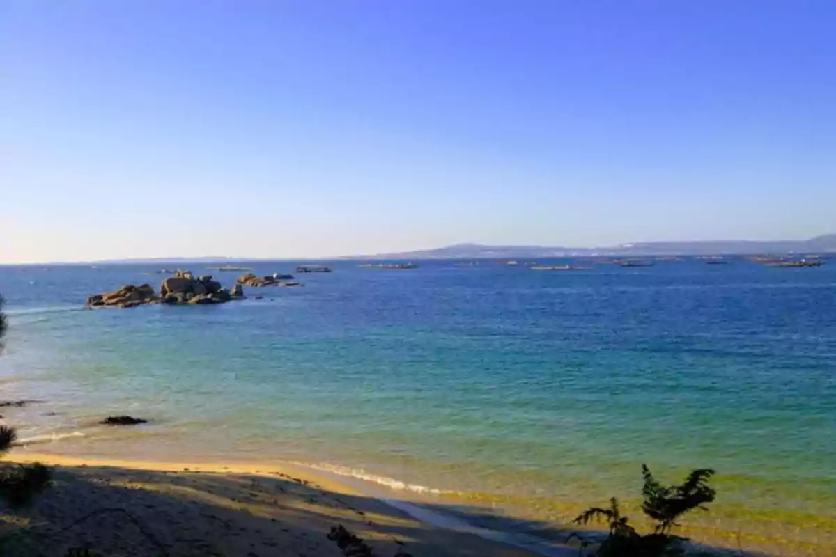 Playa con arena dorada y agua azul clara, con rocas en el mar y un cielo despejado. Playa con arena dorada y agua azul clara, con rocas en el mar y un cielo despejado.